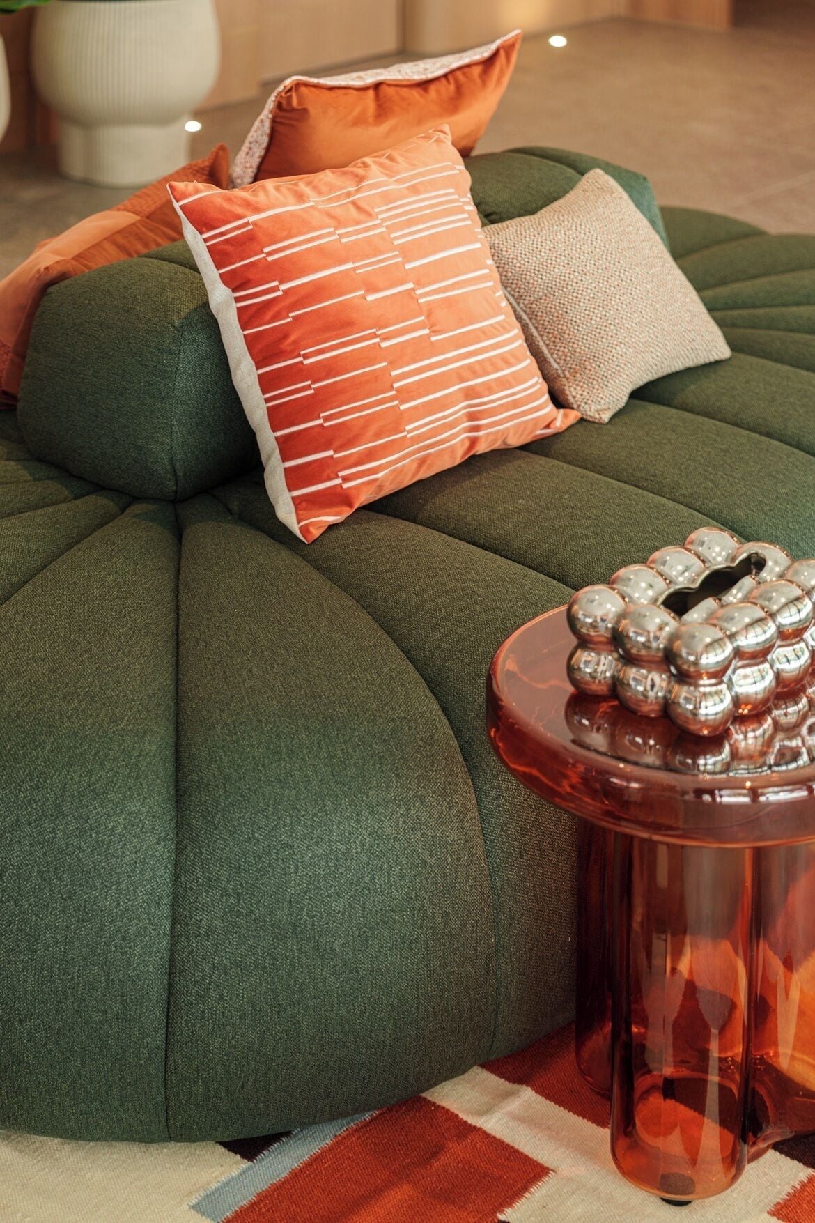 A green tufted ottoman with a round side table beside it, featuring a decorative metal object.