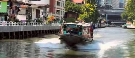 A boat moving through a waterway with buildings and a bridge in the background.