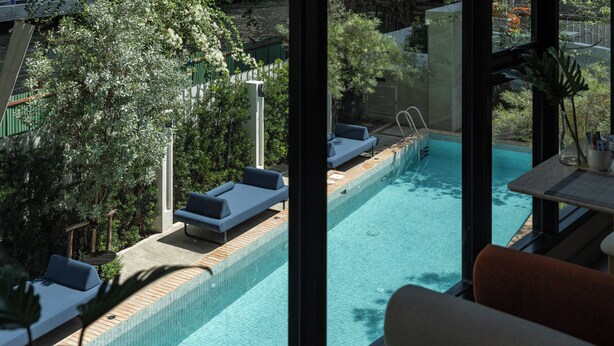 Une piscine avec des chaises longues, une terrasse en bois et une vue sur la verdure.