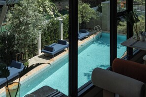 Une piscine avec des chaises longues, une terrasse en bois et une vue sur la verdure.
