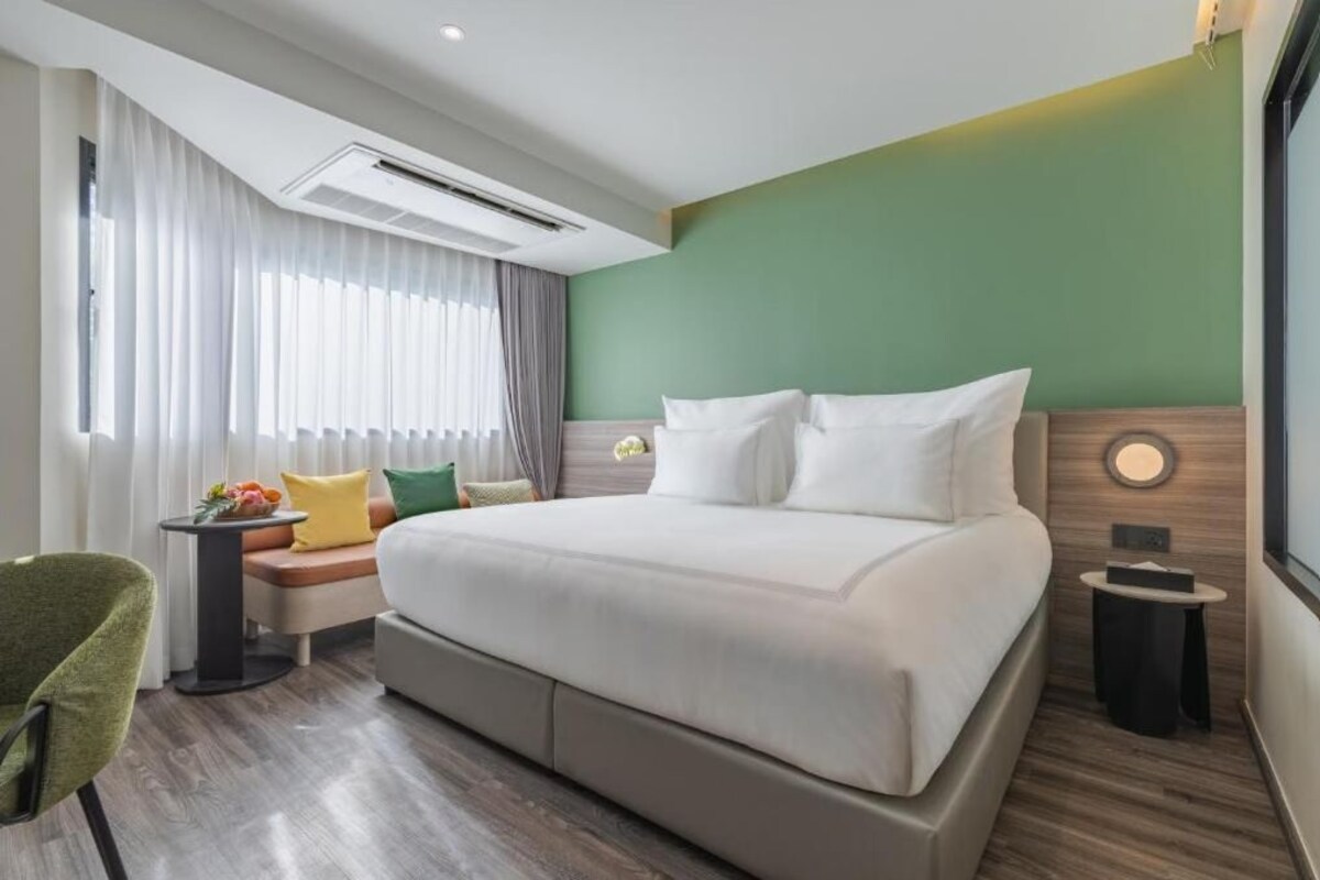 Habitación de hotel con cama, mesita de noche, una silla, ventana con cortinas e instalacion de aire acondicionado.