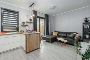 A modern living room with a sofa, a small table, and a kitchen area with a counter. - Cozy Apartment with balcony and Parking (Warszawa BIG)