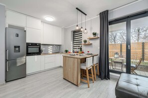 A modern kitchen with a central island, built-in appliances, and a large sliding glass door to the outdoors. - Cozy Apartment with balcony and Parking (Warszawa BIG)