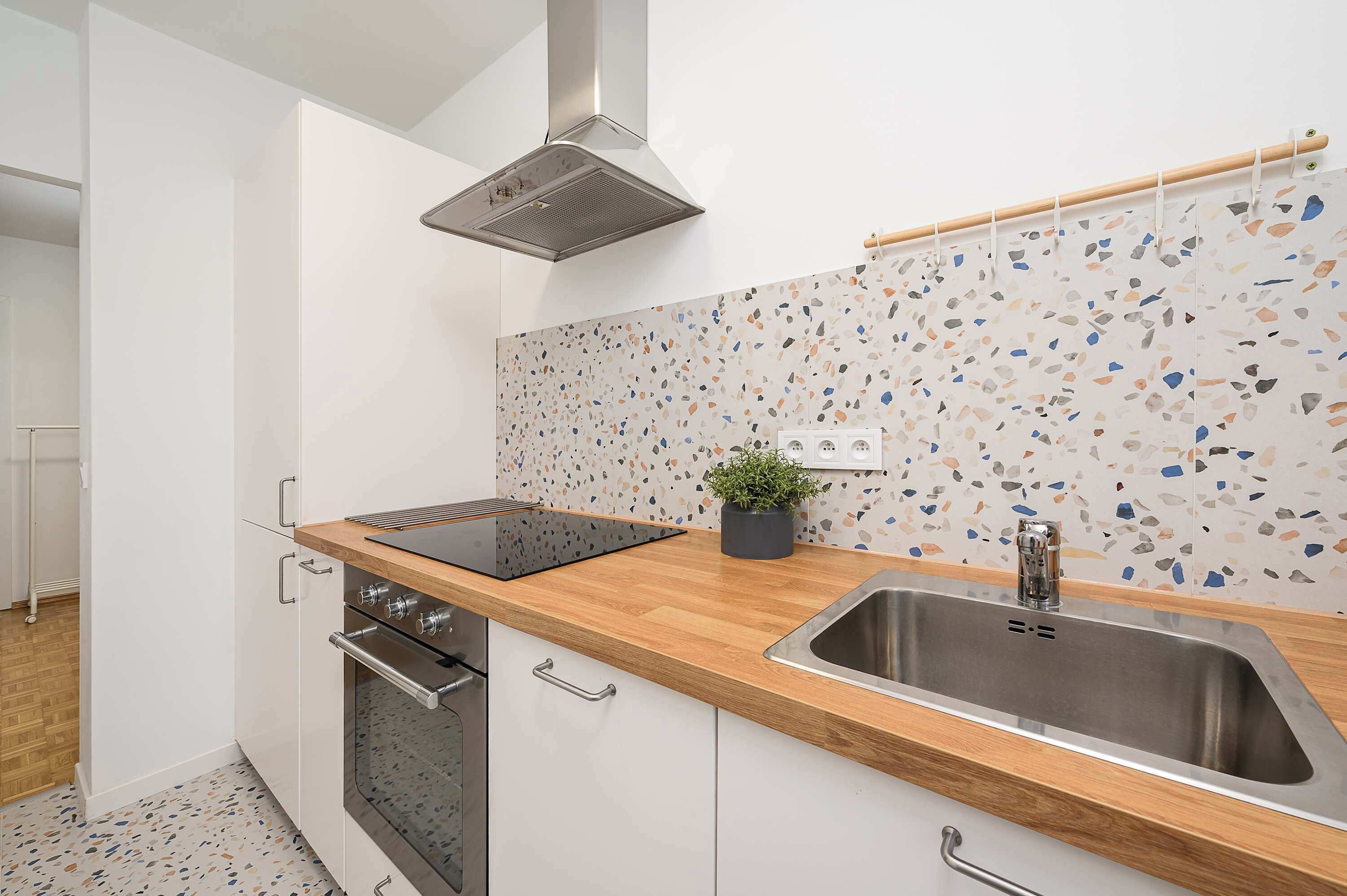 A modern kitchen with a wooden countertop, stainless steel sink, and a backsplash with a mosaic tile design.