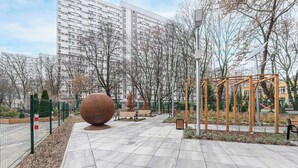 Ein gepflasterter Weg mit Bänken, einer großen, kugelförmigen Skulptur und einer hölzernen Pergola.