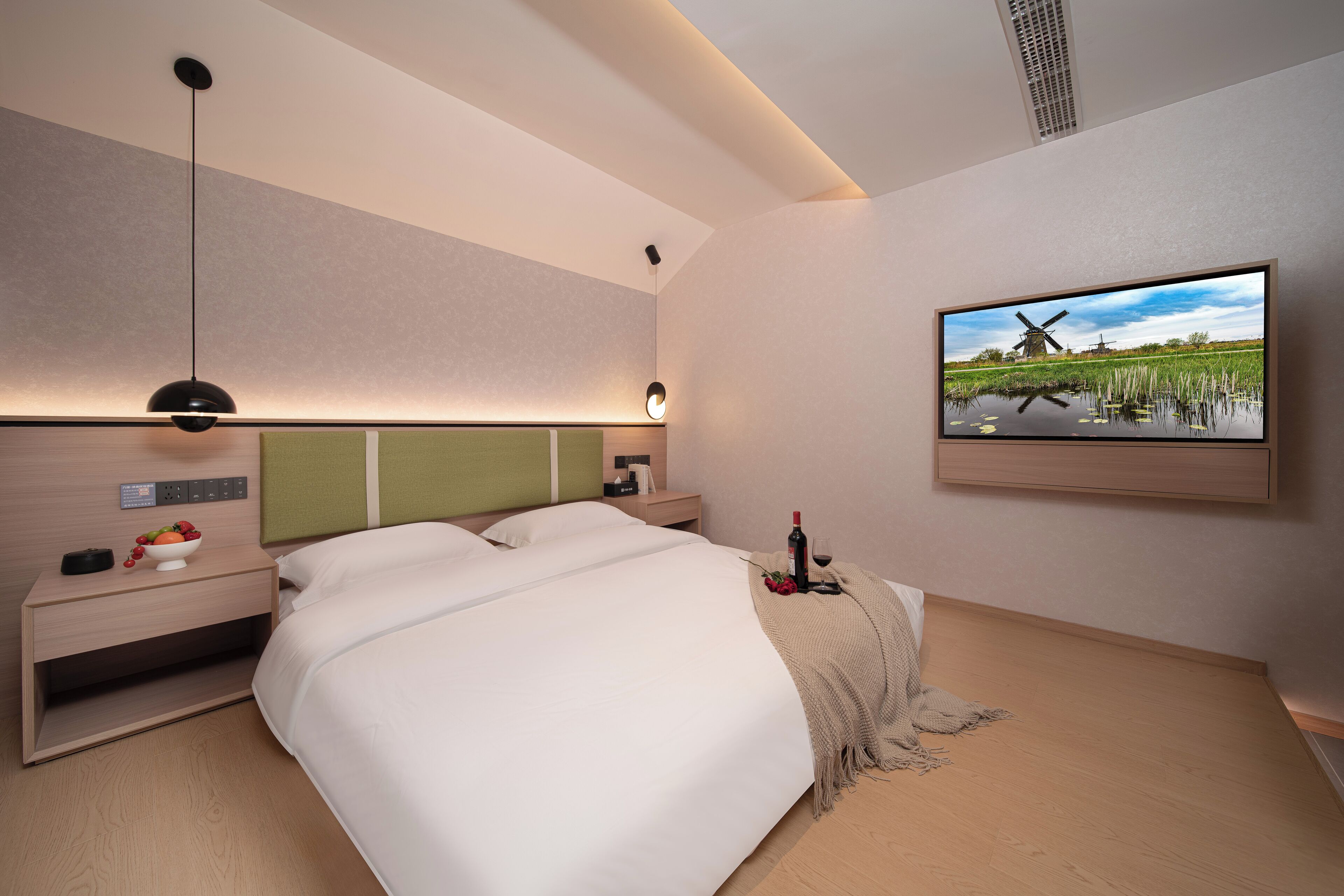 Une chambre d’hôtel moderne équipée d’un lit, d’une table de chevet, d’une lampe et d’un tableau représentant un moulin.