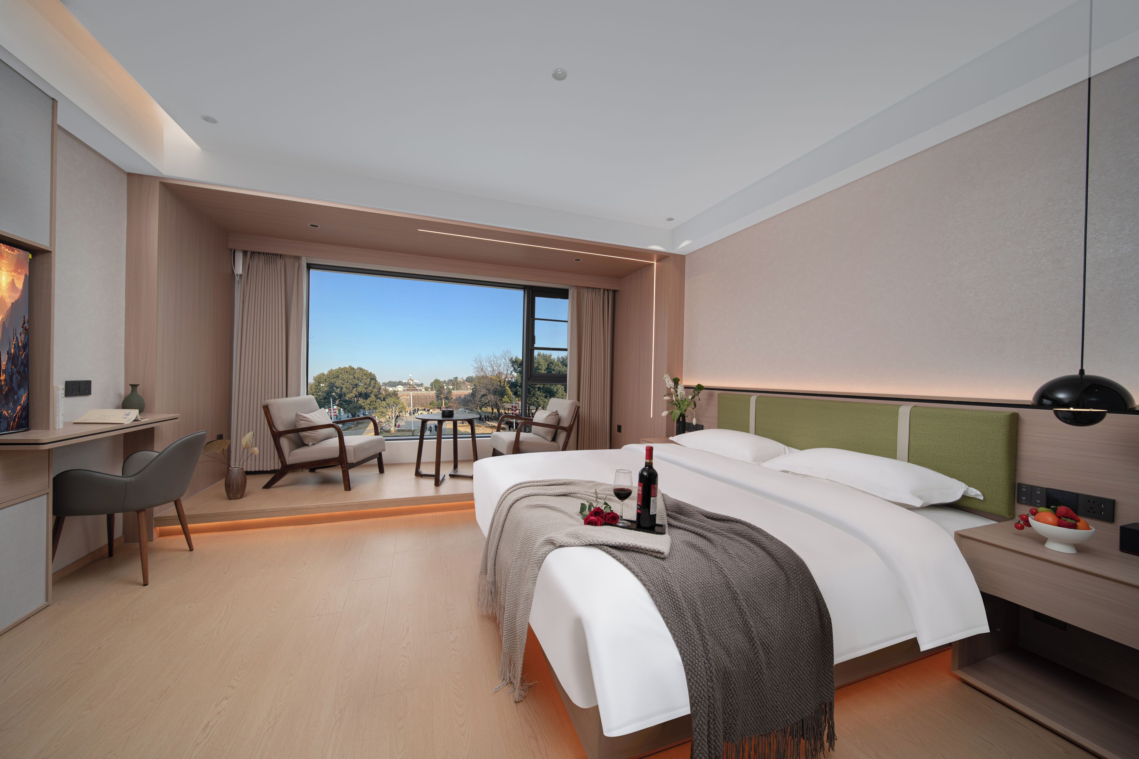 A modern hotel room with a large bed, a desk, a chair, and a view of the city.