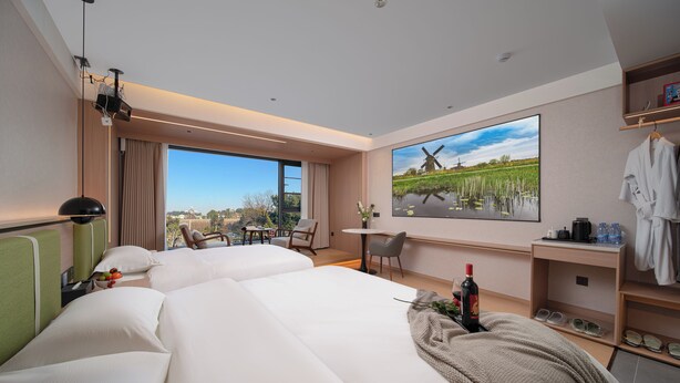 A hotel room with two beds, a desk, a chair, a large window, and a painting of a windmill. - She County Liuyue Qingshe Guesthouse  (Huangshan)