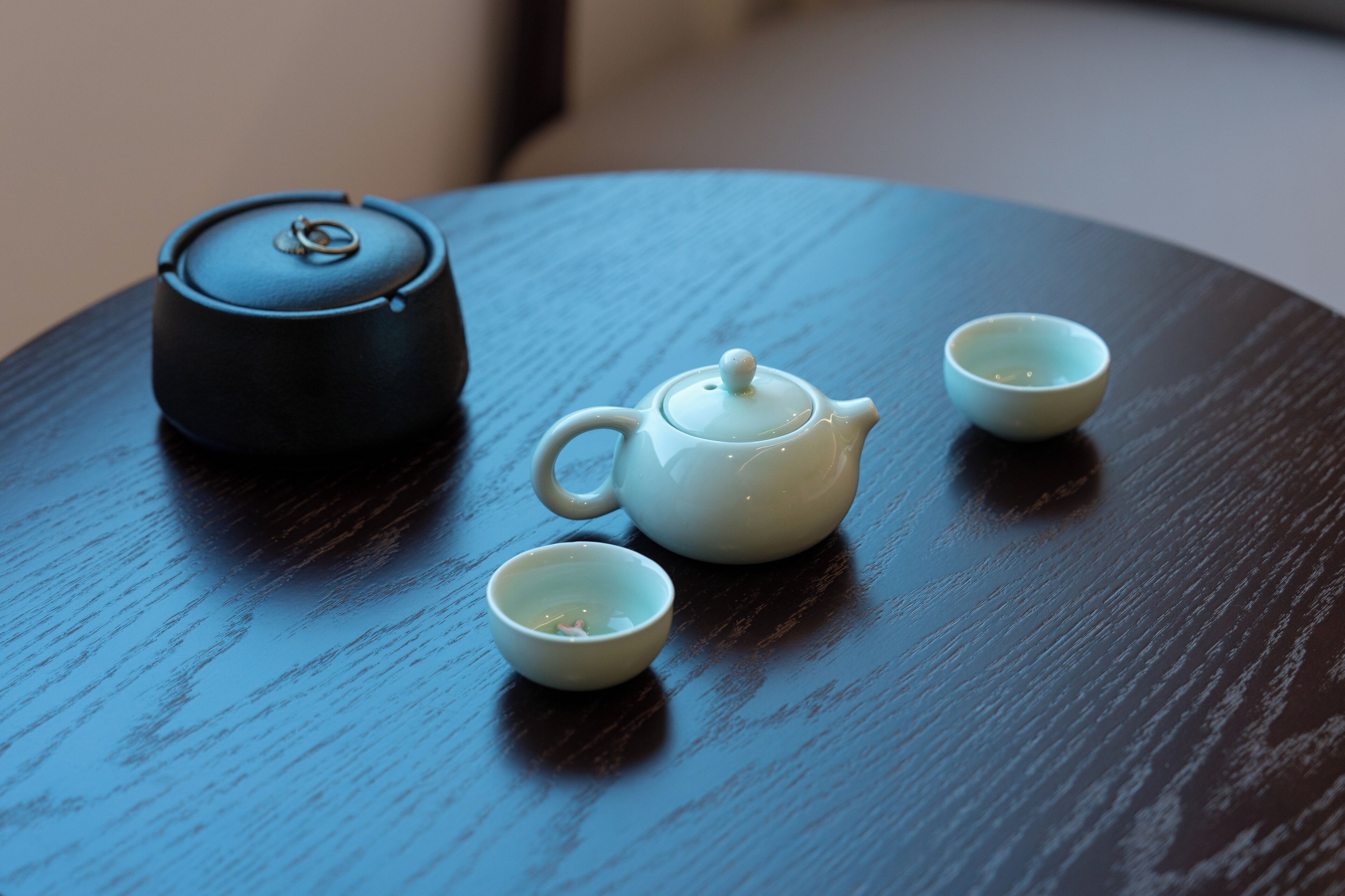 Una mesa redonda de madera con una tetera negra y dos tazas blancas.