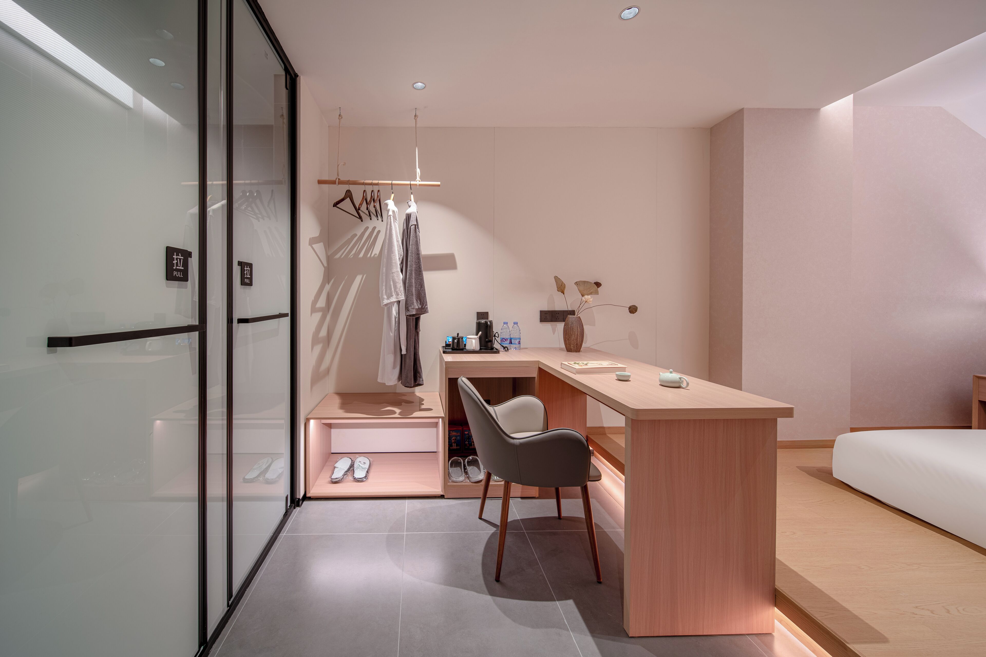 Une chambre d’hôtel moderne dotée d’une paroi en verre, d’un bureau avec une chaise, d’un lit et d’un porte-chaussures.
