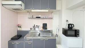 Una cocina compacta con armarios grises, un lavamanos de acero inoxidable, un microondas y un refrigerador blanco pequeño.