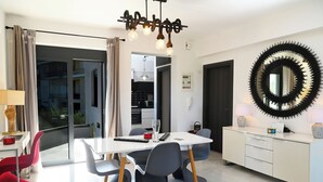 A modern dining area with a white table, grey chairs, and a red cushion. There is a large mirror on the wall and a ceiling light fixture above the table. - Hydra House Nafplio (Mili)