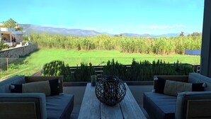 A balcony with a view of a green field and mountains. There is a wooden table with a decorative vase and two sofas with cushions. - Hydra House Nafplio (Mili)