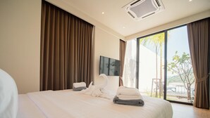 A modern hotel room with a large bed, a flat-screen TV, and a view of the outdoors through large windows. - Elegant Aileen 3 Bedroom Pool Villa Naithon (Sa Khu)
