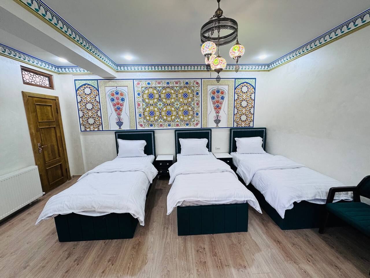 Une chambre avec trois lits simples, un plancher en bois, un lustre et des carreaux décoratifs sur les murs.