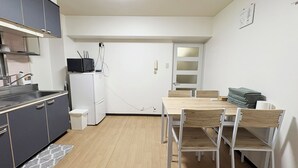 Een kleine keuken met een magnetron, koelkast en een klein spoelgedeelte. Er is een eettafel met stoelen en een stapel opgevouwen handdoeken.