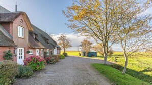 A traditional red brick house with a thatched roof, a gravel driveway, and a well-maintained garden with pink flowers. - Vacation apartment "Elsabea" in Husum-Schobüll for up to 4 people (Husum)