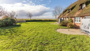 A thatched-roof house with a grassy yard and a wooden deck. - Vacation apartment "Elsabea" in Husum-Schobüll for up to 4 people (Husum)