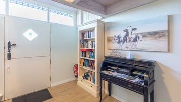 Une pièce avec une bibliothèque, un piano et un tableau représentant des vaches.