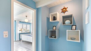 A room with light blue walls, white shelves with decorative items, a white radiator, and a white door leading to another room. - Vacation apartment "Lisa" in Husum-Schobüll for up to 2 people (Husum)