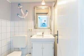 Une salle de bain avec un lavabo blanc, des toilettes et un miroir doté d’un cadre orné.