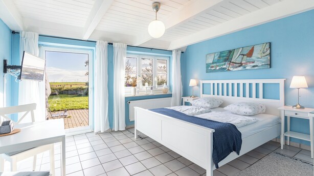A bedroom with a bed, a desk, a chair, a window with curtains, and a view of the outdoors. - Vacation apartment "Lisa" in Husum-Schobüll for up to 2 people (Husum)