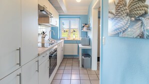 A kitchen with white cabinets, a window with a view of the outdoors, and a trash bin. - Vacation apartment "Lisa" in Husum-Schobüll for up to 2 people (Husum)
