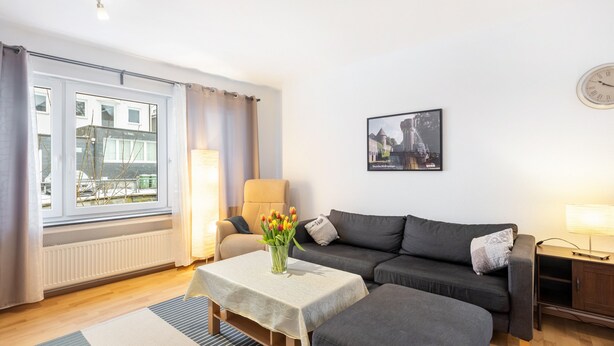 Een woonkamer met een bank, een tafel met een bloevas, een lamp en een ingelijst schilderij aan de muur.