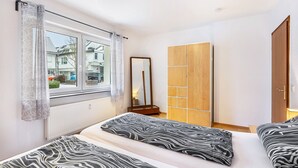 Een slaapkamer met twee bedden, een raam met gordijnen, een spiegel en een kledingkast.