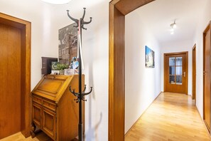 A hallway with wooden flooring, a coat rack, a wooden cabinet, and a door with a frosted glass panel.