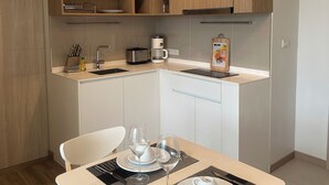 A modern kitchen with wooden cabinets, a built-in microwave, and a coffee maker. There is a dining table set with plates, glasses, and cutlery. - Laguna Lake View Condo with Rooftop Pool – Skypark Bang Tao (ตำบลเชิงทะเล)
