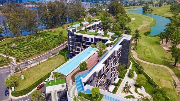 A modern hotel with a pool, surrounded by lush greenery and a golf course. - Laguna Lake View Condo with Rooftop Pool – Skypark Bang Tao (ตำบลเชิงทะเล)