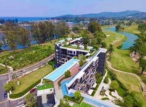 A modern hotel with a pool, surrounded by lush greenery and a golf course. - Laguna Lake View Condo with Rooftop Pool – Skypark Bang Tao (ตำบลเชิงทะเล)