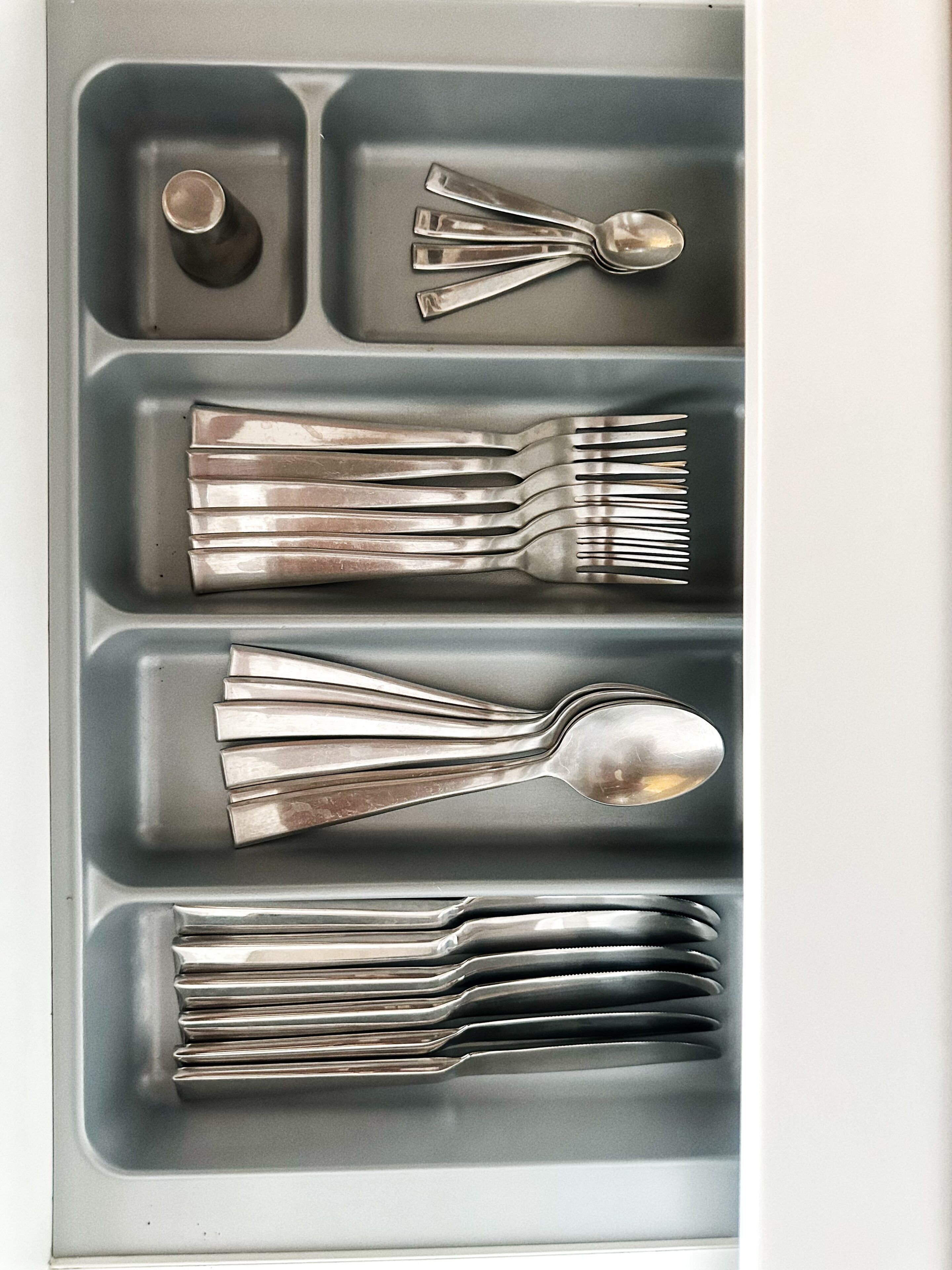 Un cajón con cubiertos de plata, incluyendo tenedores, cucharas y una taza.