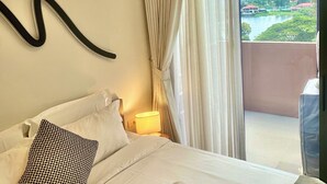 A hotel room with a bed, a wall-mounted light, a view of a lake and mountains, and a swan towel art on the bed. - Laguna Lake View Condo with Rooftop Pool – Skypark Bang Tao (ตำบลเชิงทะเล)