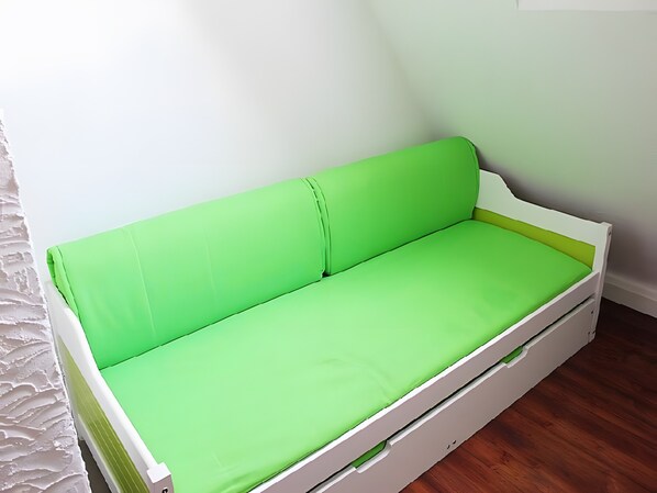 A single-bed room with a green mattress, white headboard, and wooden flooring.