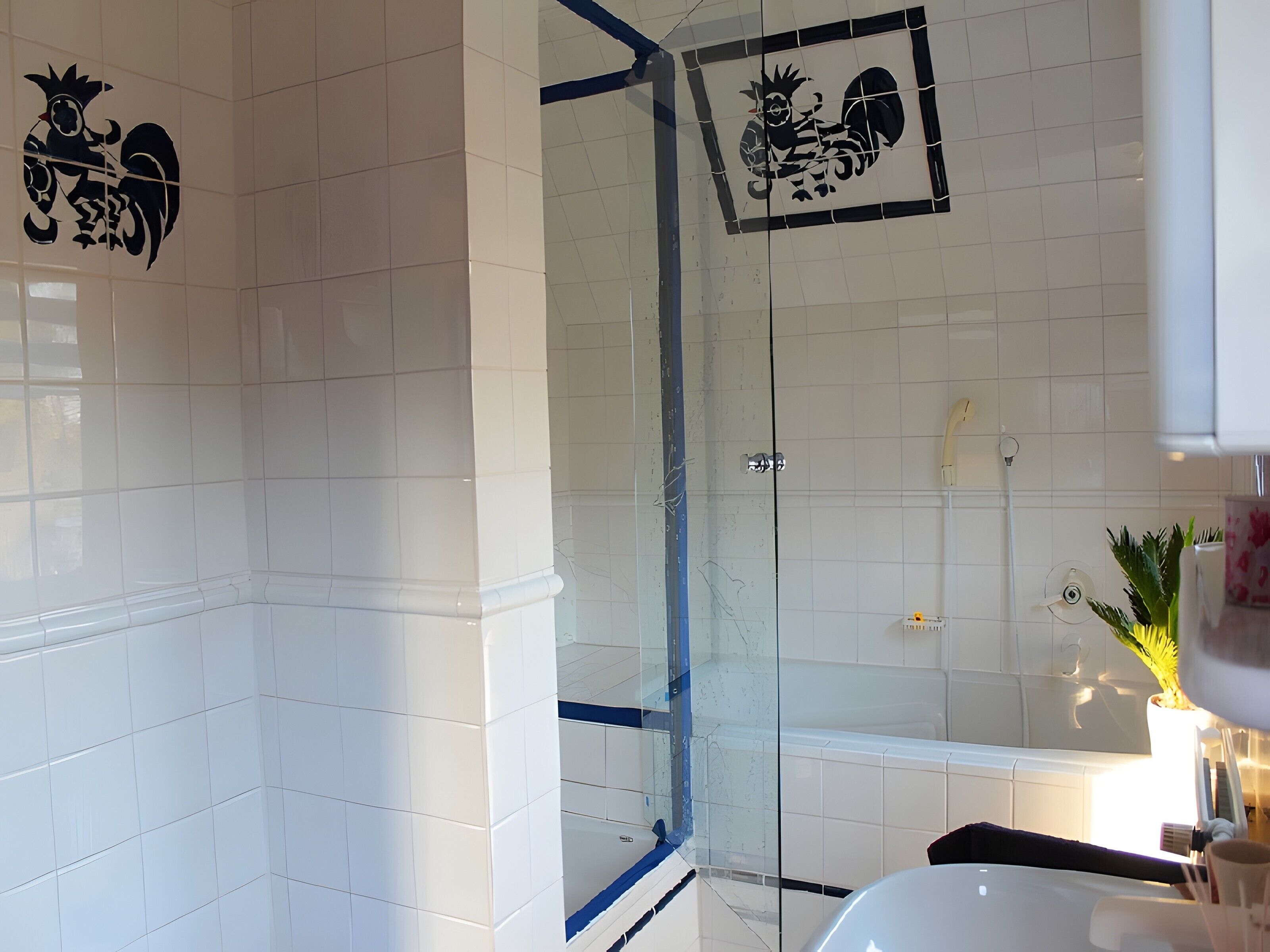 A bathroom with white tiles, a glass shower enclosure, and a decorative rooster emblem on the wall.