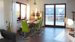 A modern dining area with a wooden table, green chairs, and a view of the outside through a large sliding door. - Holiday Home 'Dell, 99qm' with Shared Pool, Shared Terrace and Wi-Fi (Möhnesee)
