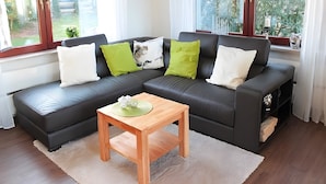 A modern living room with a sectional sofa, a wooden coffee table, and large windows offering a view of the outdoors. - Holiday Home 'Dell, 99qm' with Shared Pool, Shared Terrace and Wi-Fi (Möhnesee)