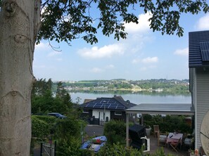 A residential area with a house featuring solar panels, a covered patio, and a view of a lake and distant buildings.