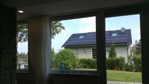 Una stanza con ampie finestre, un muro in pietra e vista su una casa con pannelli solari.