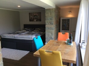 Une chambre à coucher avec un lit, une table sur laquelle se trouve une bouteille, et une chaise.