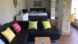 Un soggiorno moderno con un divano nero, un tavolino in legno e un letto con testiera.