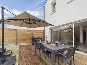 Eine Terrasse mit Tisch, Stühlen, einem Grill und einem Sonnenschirm.