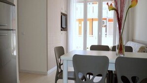 A modern kitchen with a refrigerator, a dining table with chairs, and a large window with a view of a building outside. - Modern seaside home in Bibione (Bibione)