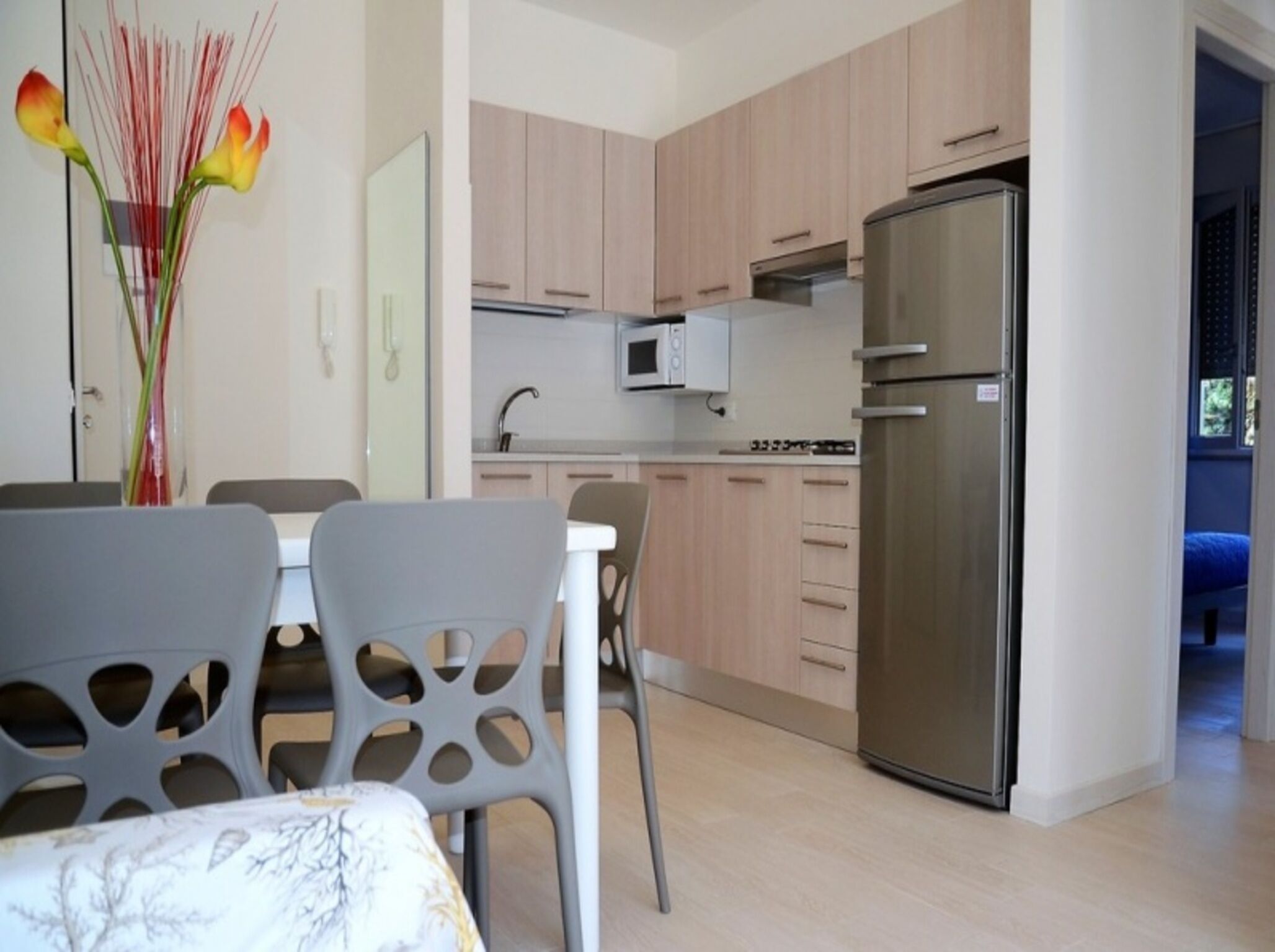 A modern kitchen with light wood cabinets, a stainless steel refrigerator, and a microwave.