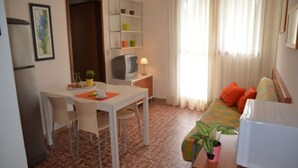 A compact living space with a dining area, a television, a sofa with cushions, and a window with curtains. - House with seaview terrace - Beahost (Bibione)