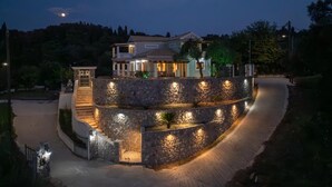 A two-story house with a stone retaining wall, a driveway, and a small staircase leading to the entrance. - Villa Logas Hill with Panoramic Sea Views, Wi-Fi and Air Conditioning (Peroulades)