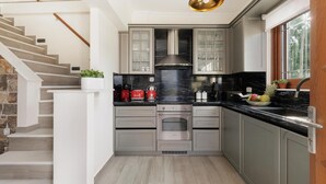 A kitchen with grey cabinets, a black countertop, a stainless steel range hood, and a wooden staircase. - Villa Logas Hill with Panoramic Sea Views, Wi-Fi and Air Conditioning (Peroulades)