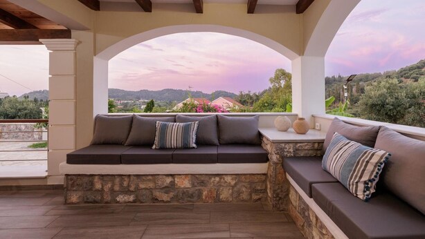 A covered outdoor seating area with stone walls, a cushioned bench, and a view of the landscape. - Villa Logas Hill with Panoramic Sea Views, Wi-Fi and Air Conditioning (Peroulades)